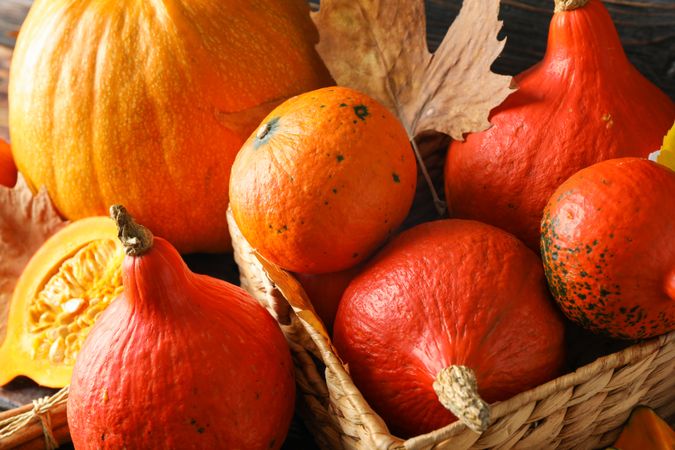 Pumpkins in straw basket on wooden background, closeup