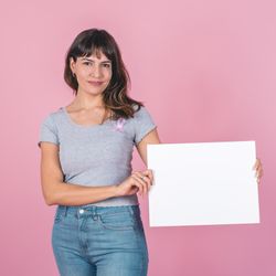 A woman wearing a pink breast cancer awareness ribbon holding a blank sign against a pink background