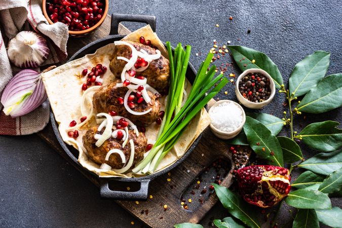 Looking down at Georgian plate of abkhazura meat cutlets with pomegranate seeds, bay leaves & onions