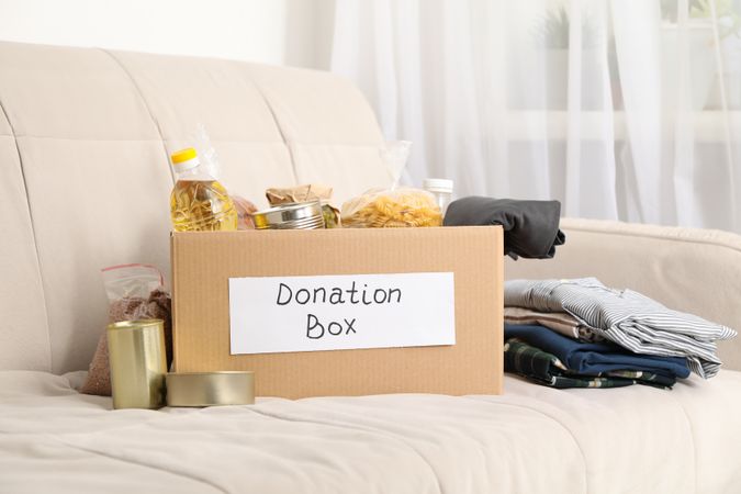 Donation box. Food and clothes on sofa. Volunteering