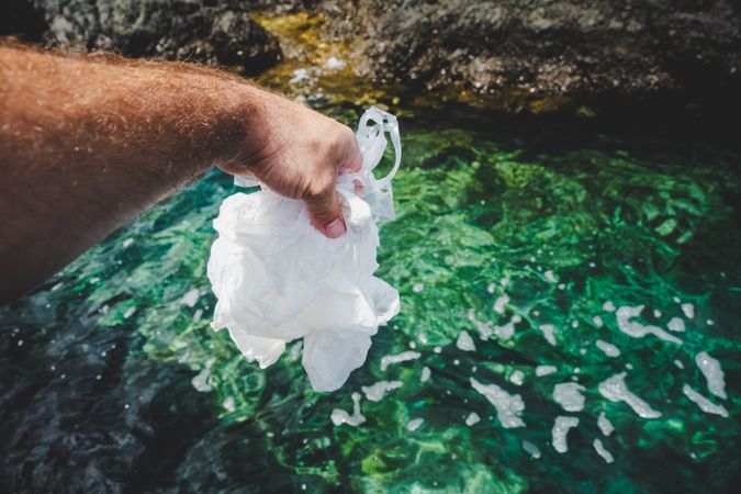 Crop man pulling plastic bag out of water