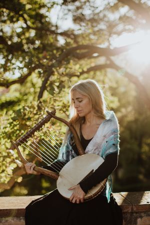 Sensual female musician playing lyre in garden