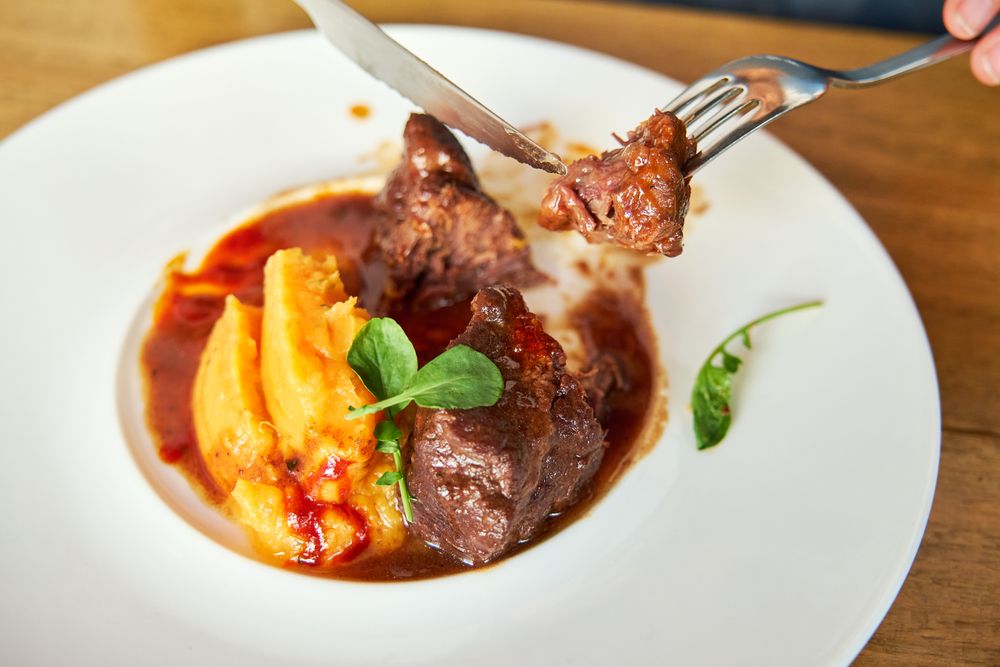 Detail of a person grabbing a piece of a meat cut from a dish of