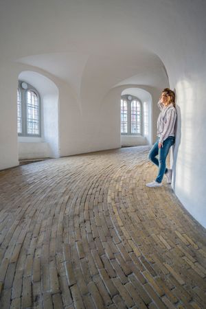 Casual woman leaning on wall in spacious gallery with windows