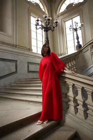 Portrait of woman in red dress standing on staircase of historic building