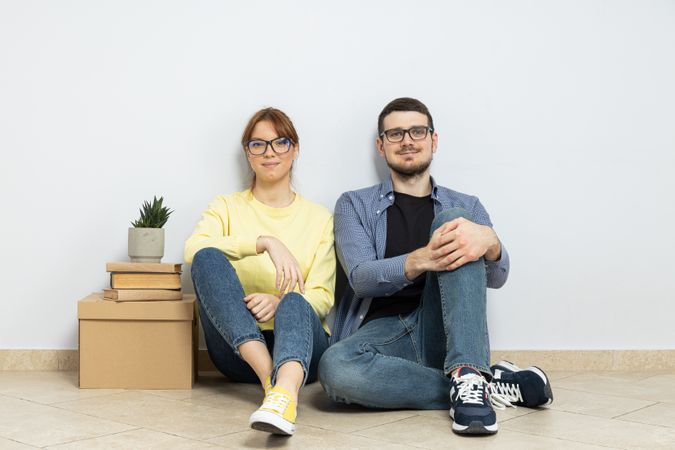 A couple is sitting on the floor in an empty apartment, with boxes