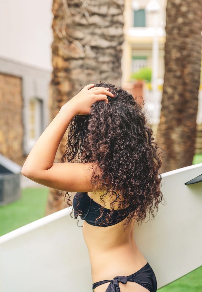 Brunette surfer woman in bikini holding a surfboard with hand to her hair