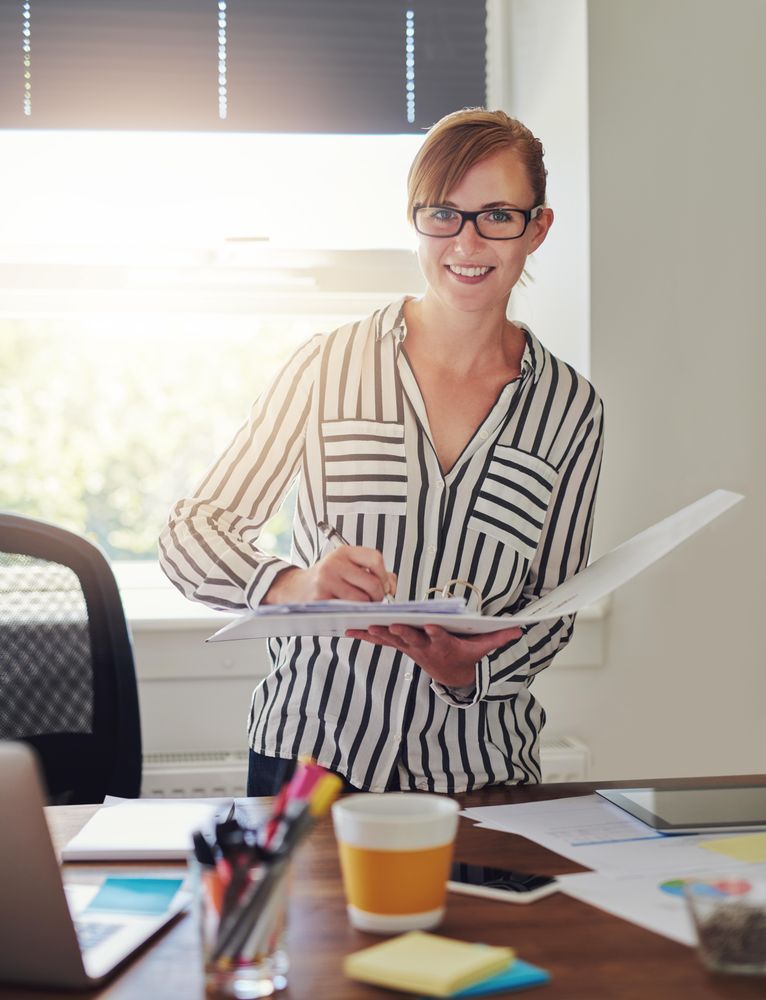 Smiling female in striped shirt looking through binder in her home office, vertical