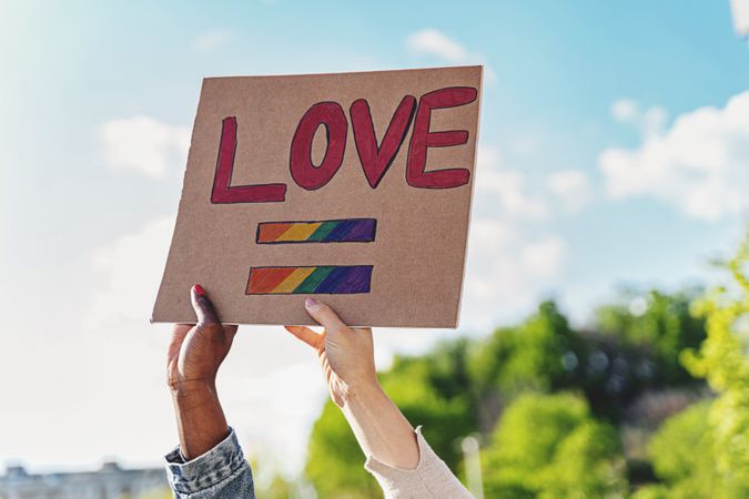 Diverse female hands holding a handmade cardboard sign with "Love" written on it