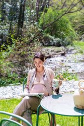 Smiling pregnant young woman reading newspaper outside
