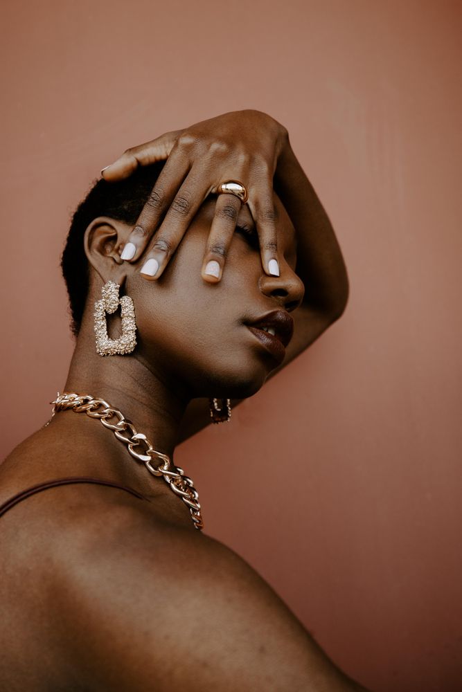 Woman wearing gold necklace and gold ring and gold earring against brown background