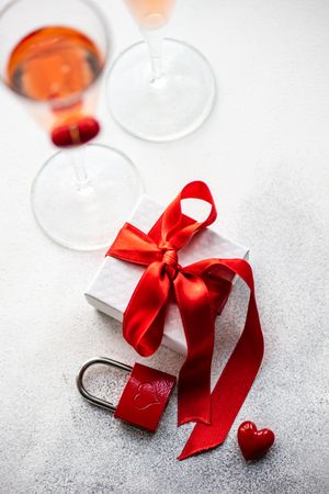 Red ribbon wrapped gift with padlock and pink champagne
