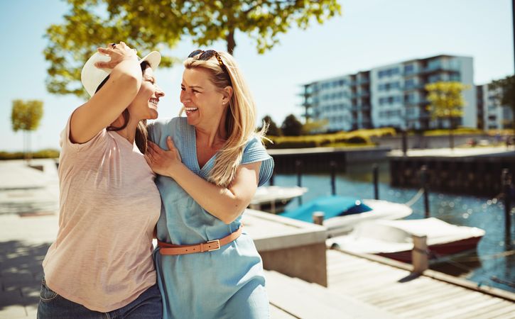 Two women laughing and holding each other on sunny day near the river, copy space