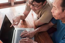 Happy adult son teaching older father using laptop
