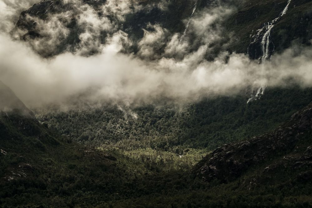 Clouds over green valley between gray mountains