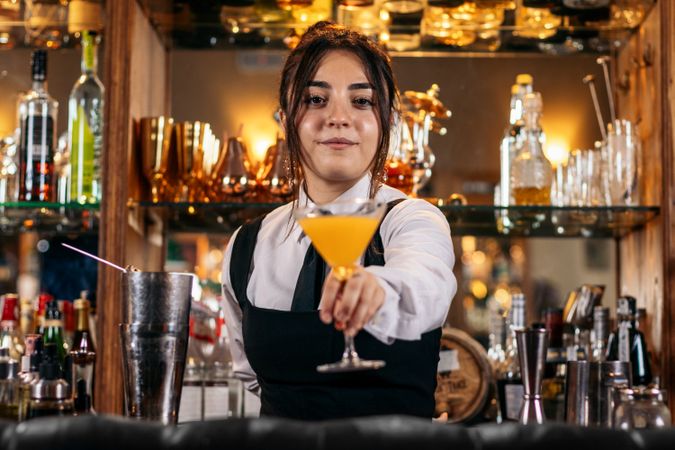 Young female bartender offering a drink