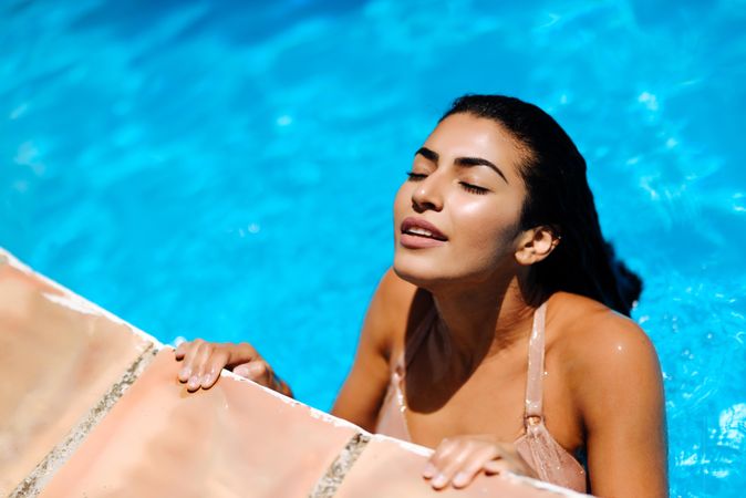 Beautiful Arab woman grasping side of swimming pool with eyes closed