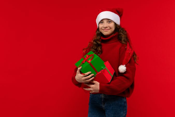 Smiling girl in Santa hat holds multiple Christmas gifts.