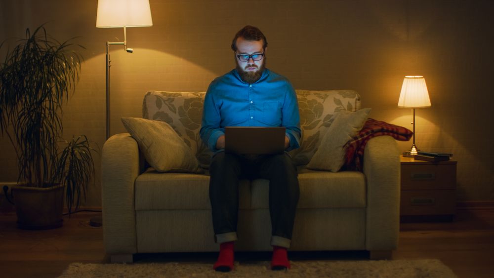 Portrait Shot of a Man Sitting on a Couch in His Living Room, Laptop on His Knees.