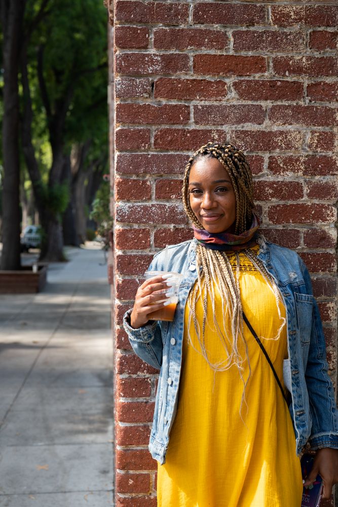 Portrait of woman with box braids standing in front of brick wall smiling and looking at camera