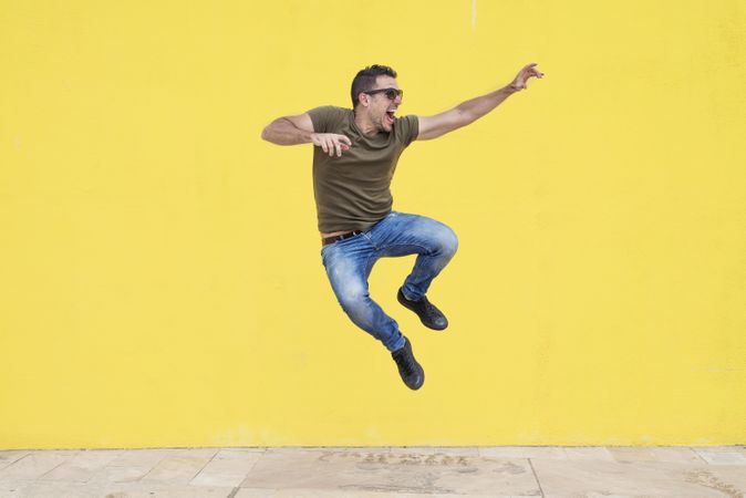 Happy male jumping in front of yellow wall and looking to the side