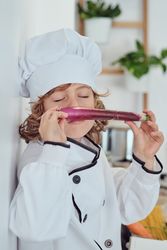 Adorable preteen boy sniffing fresh red leek in kitchen