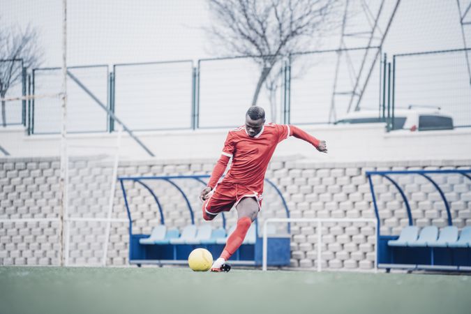 Black soccer player with red outfit playing soccer.