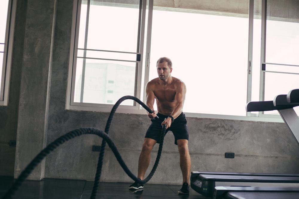 Intense muscular man training with ropes in gym