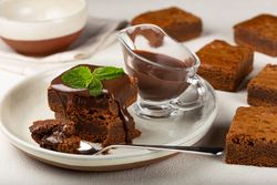 Brownies on plate with spoon served with sauce and mint garnish