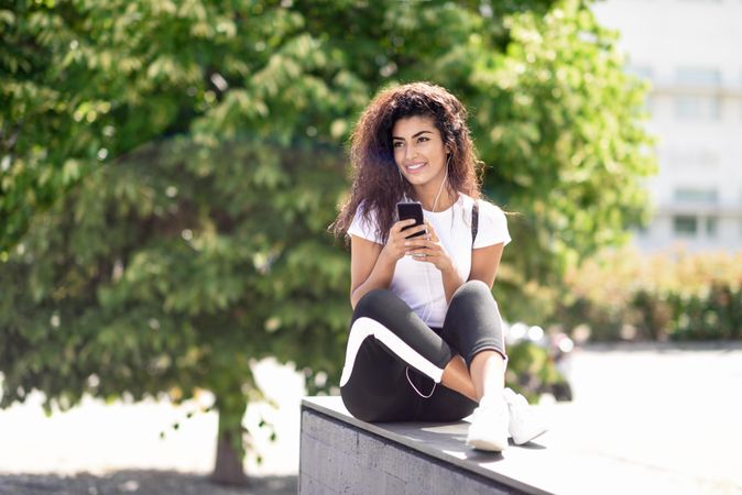 Arab woman with phone and earphones sitting outdoors