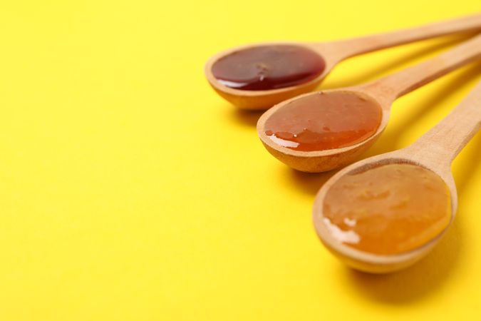 Spoons with jam on yellow background, space for text