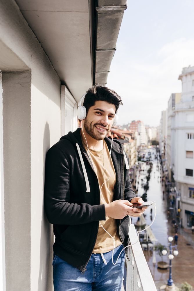 Young happy man holding smartphone on balcony