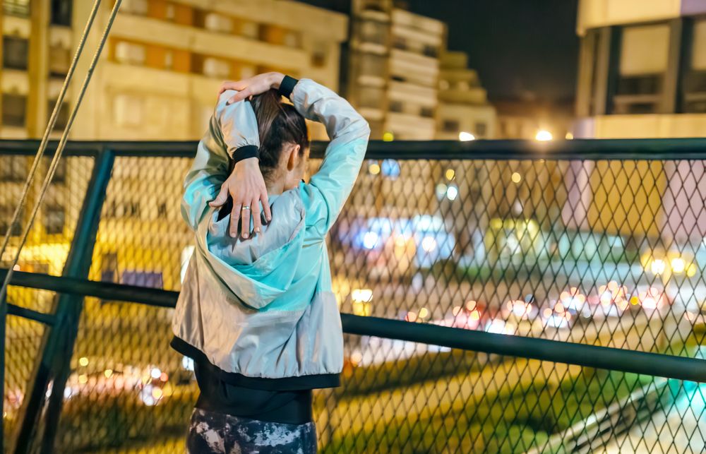 Unrecognizable athletic woman stretching her arms before run on the city at night