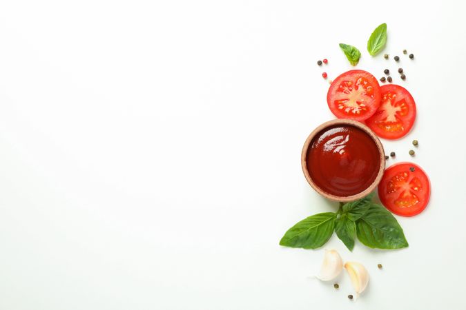 Flat lay composition with fresh cherry tomatoes slices, basil, pepper, garlic and sauce on plain background, space for text. Ripe vegetables