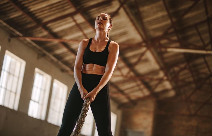 Woman exercising with battling rope at old warehouse