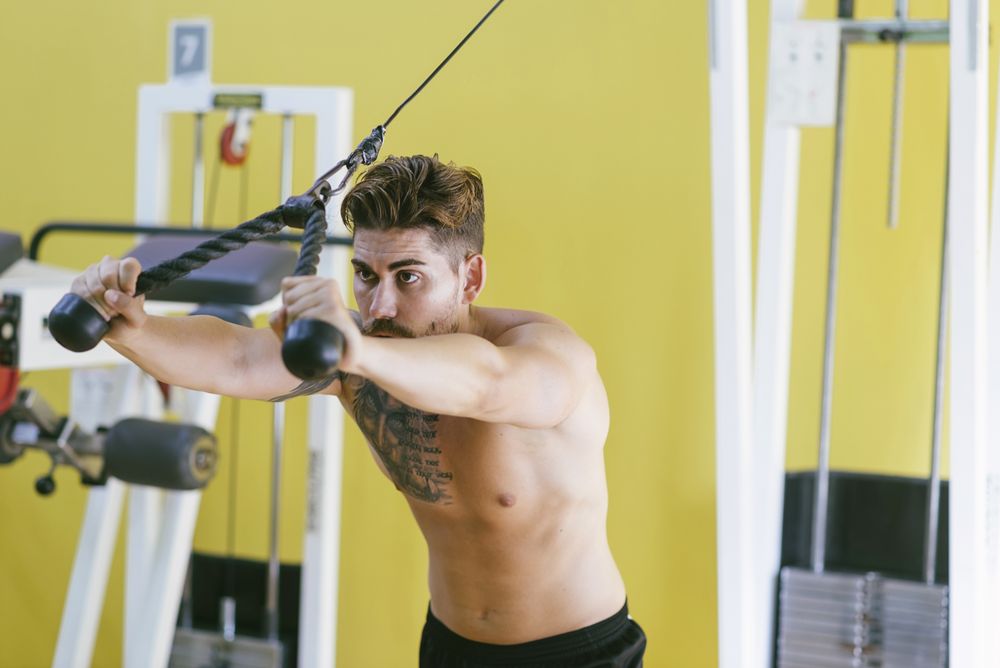Healthy male in gym working out his arms using weights machine