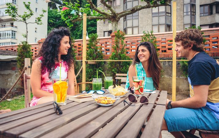 Friends sitting at table in backyard with cocktails and snacks