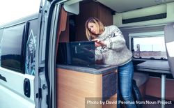 Woman in warm sweater cleaning while standing in back of van 0J8M84