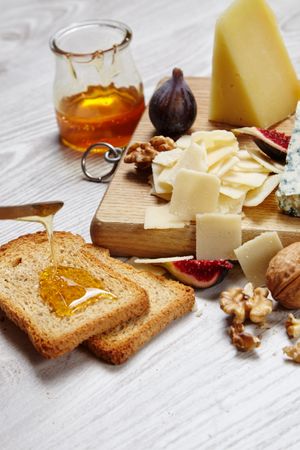 Cheese plate on wooden board with toast and honey, vertical