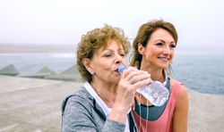 Older sportswoman drinking water with female coach