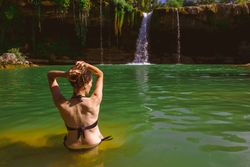 Anonymous woman touching hair and looking at waterfall