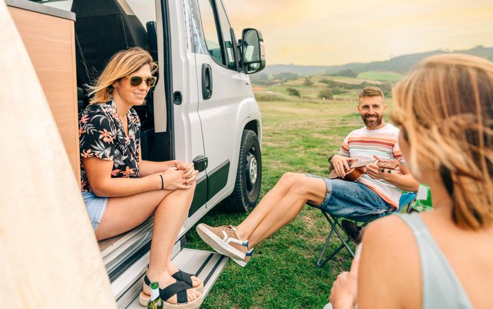 Three people sitting outside their motorhome in a scenic location