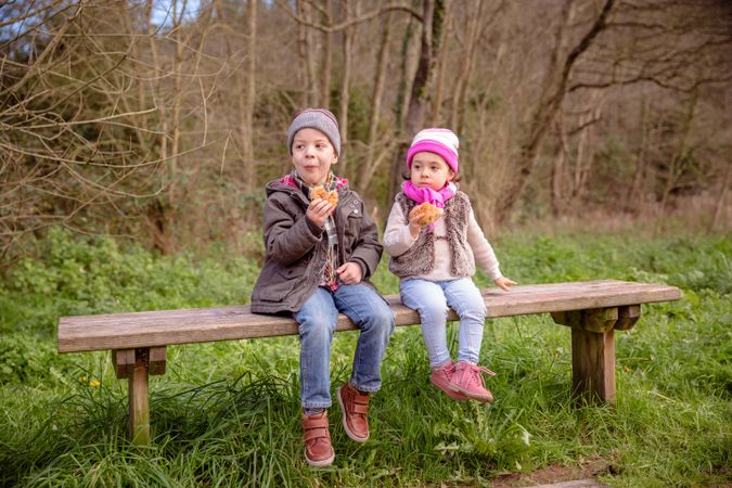 Little boy and girl sitting on park bench with snack