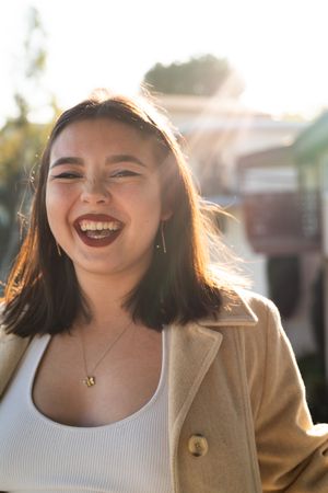 Fashionable young woman laughing looking at camera with sun rays behind