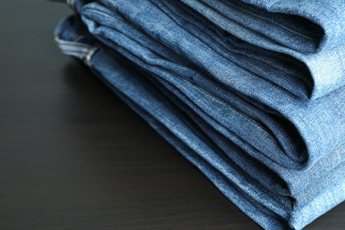 Stack of jeans pants on table, space for text