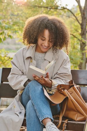 Smiling Black Latina woman reading book in park