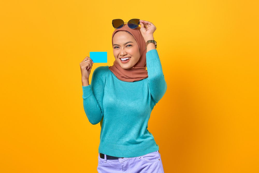 Muslim woman looking happy with credit card and adjusting sunglasses