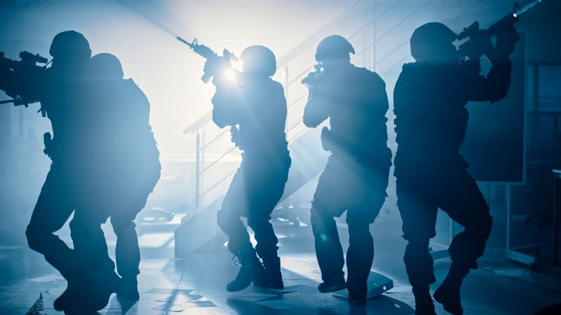 Masked Team of Armed SWAT Police Officers Move in a Hall of a Dark Seized Office Building with Desks and Computers.