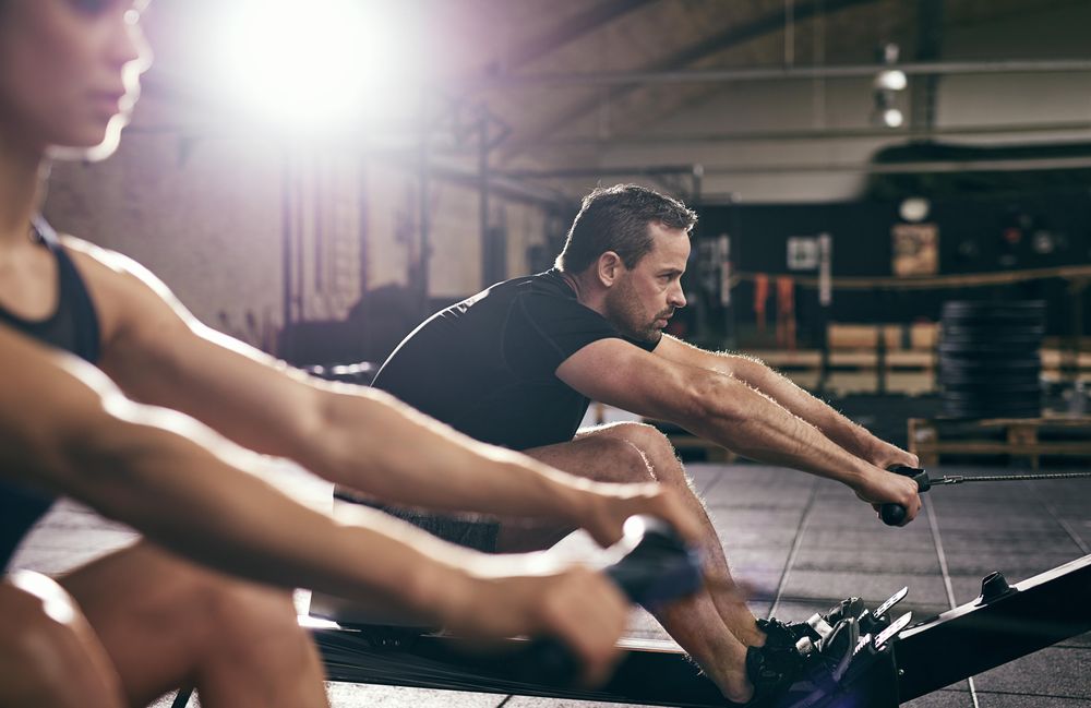 Two fit adults exercising, focus on male pulling oar on row machine