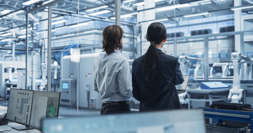 Young Engineer and Asian Technician Having a Conversation and Using a Laptop Computer. Specialists Monitoring, Analyzing Conditions at a Modern Electronics Factory with Automated Conveyor